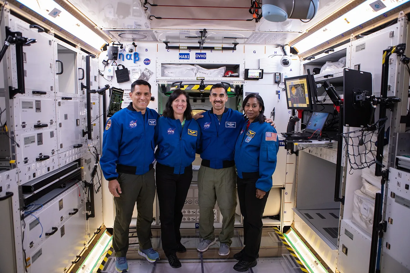 Group of four NASA astronauts and candidates standing inside the LOP-G space station training module at the SSPF