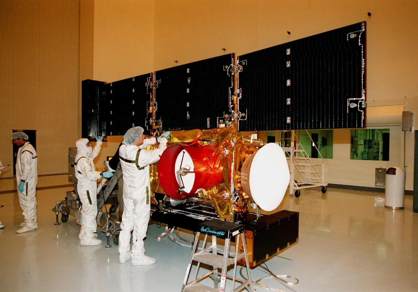 "In the Payload Hazardous Servicing Facility, workers adjust the solar panels of the Stardust spacecraft before performing lighting tests. "