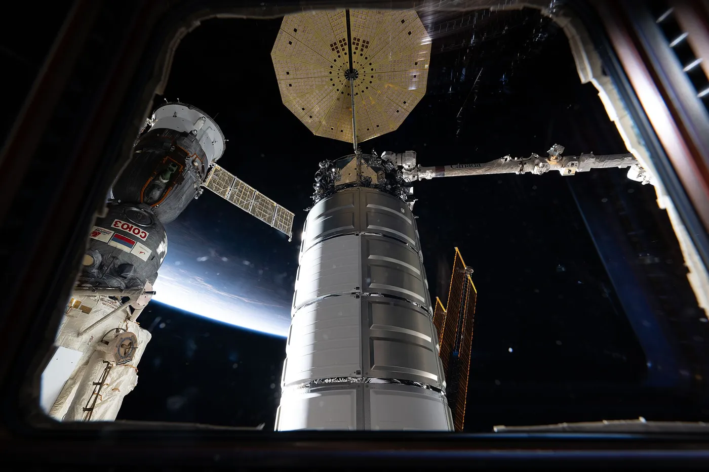 Two spacecraft attached to the International Space Station are seen through a window in the cupola