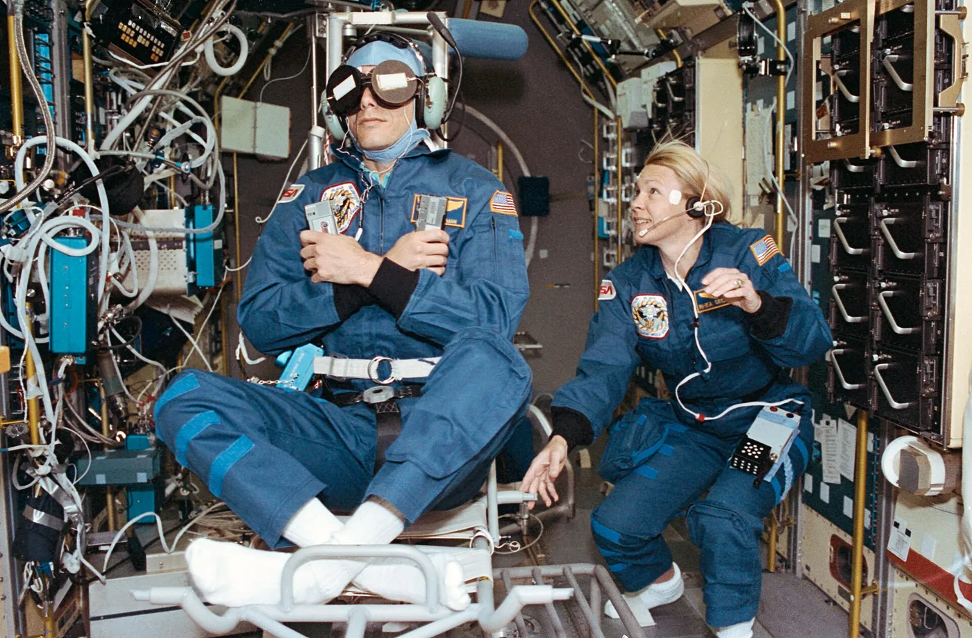STS-58 Payload Commander Rhea Seddon spins the Spacelab Life Sciences rotating chair as Payload Specialist Martin Fettman serves as a test subject…
