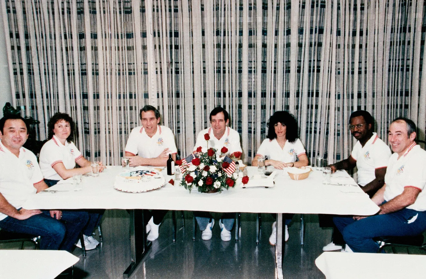STS-51-L astronauts Onizuka, left, McAuliffe, Smith, Scobee, Resnik, McNair, and Jarvis enjoy the traditional prelaunch breakfast.