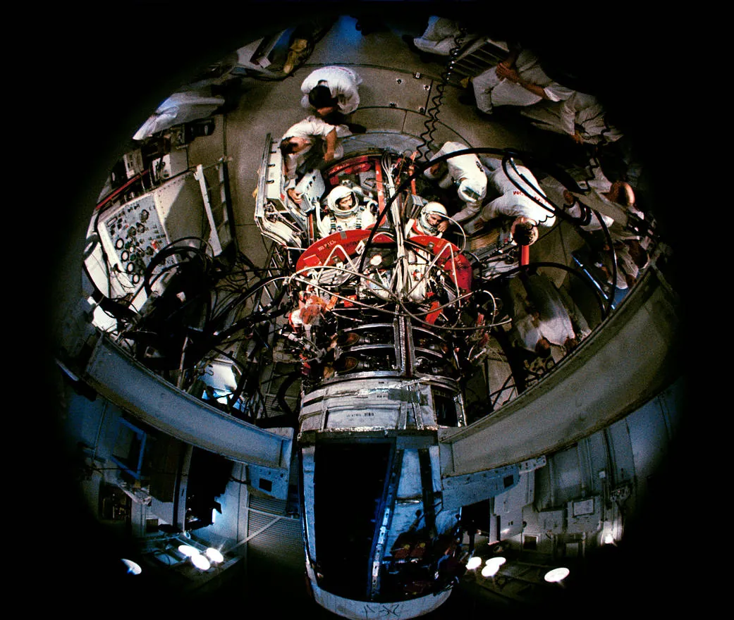 A fisheye lens looks down into the open spacecraft as pad technicians settle the crew into their seats atop the rocket.