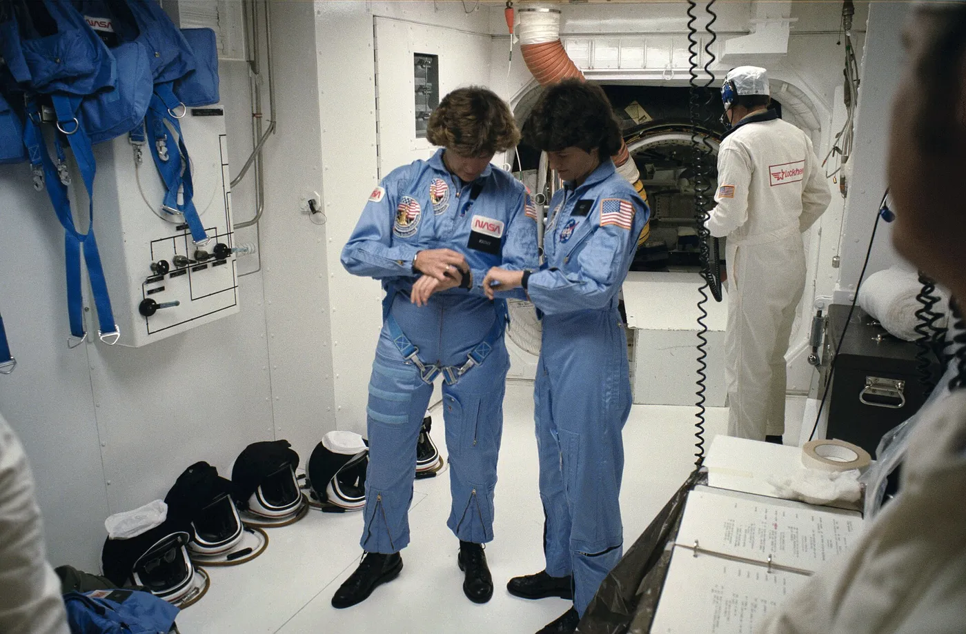 Astronauts Sally K. Ride (right) and Kathryn D. Sullivan, two of three mission specialists, synchronize their watches prior to ingressing the Space…