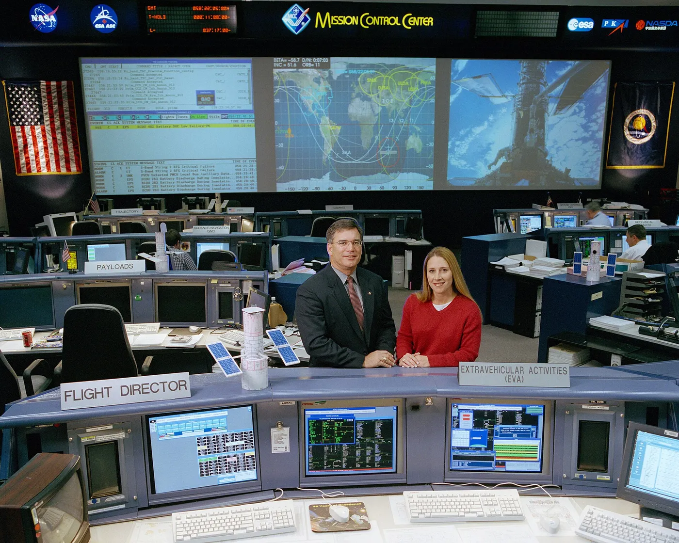 Bryan P. Austin, lead flight director for STS-109, and Dana Weigel, lead EVA officer, pose near their respective consoles in the Shuttle Flight…