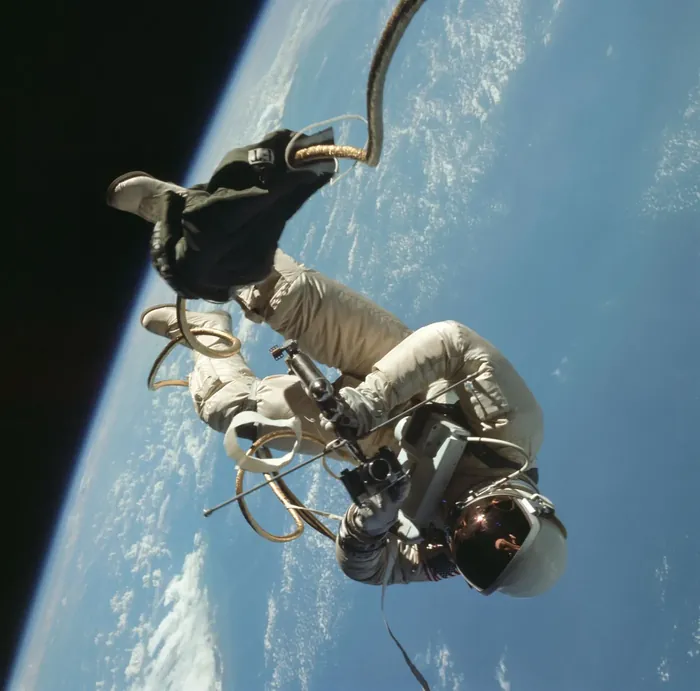 White drifts above a cloud-covered Earth, umbilical and tether trailing behind him.