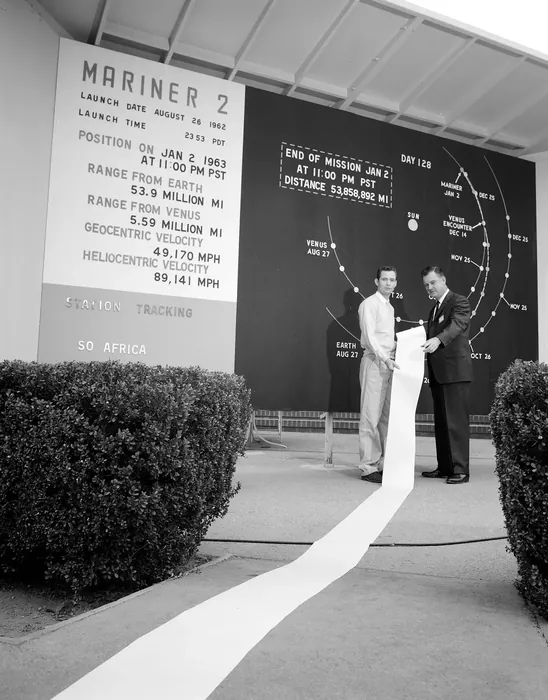 A long scroll of data from Venus, seen in front of JPL's Mariner 2 mission board.