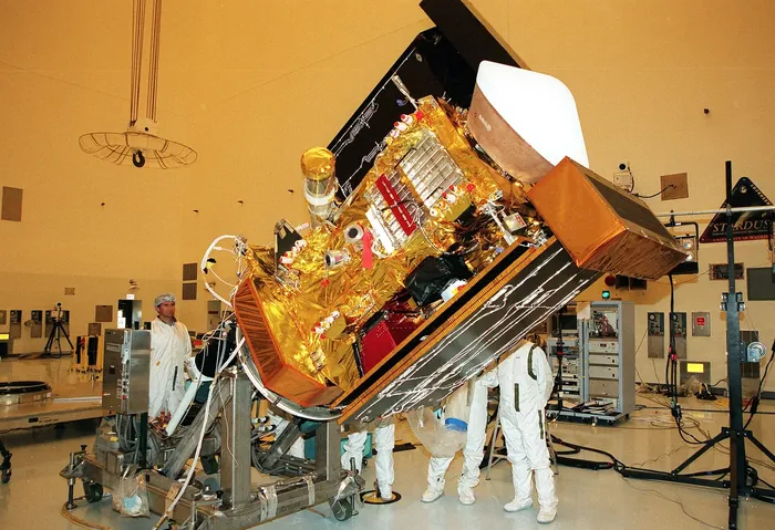 Workers in the Payload Hazardous Servicing Facility watch as the Stardust spacecraft is lowered before deploying panels for lighting tests.