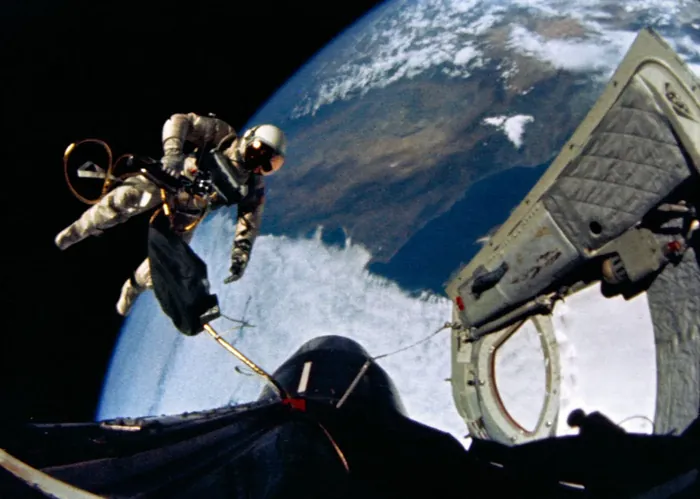White floats beside the spacecraft, the open hatch and its umbilical in view.