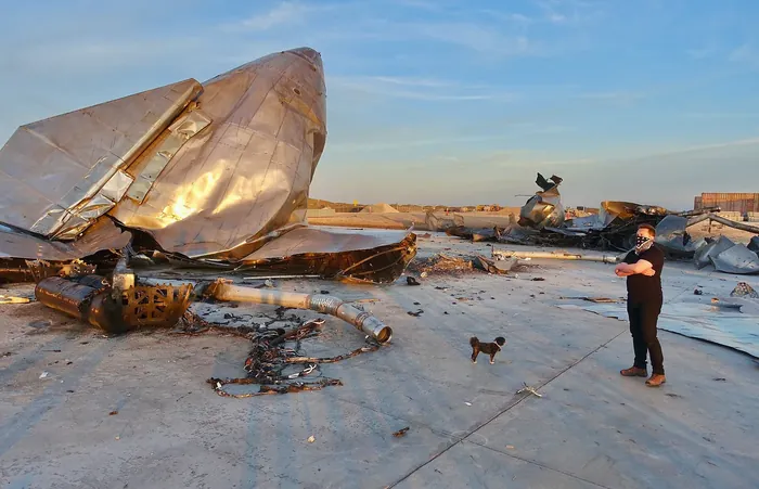 Starship SN8 wreckage. A long contemplative gaze at the sun-splashed sculpture on the landing pad. Also Elon’s dog is present.