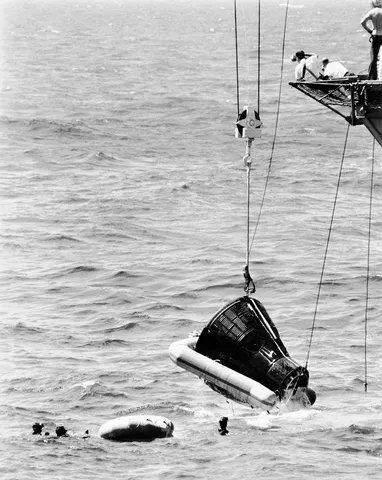 The Gemini-4 Astronauts is shown being hoisted aboard the Aircraft Carrier USS Wasp. The flotation collar is still attached to the spacecraft.…
