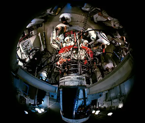 A fisheye lens looks down into the open spacecraft as pad technicians settle the crew into their seats atop the rocket.