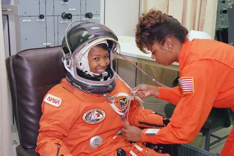 NASA astronaut Mae Jemison waits as her suit technician, Sharon McDougle, performs a unpressurized and pressurized leak check on her spacesuit